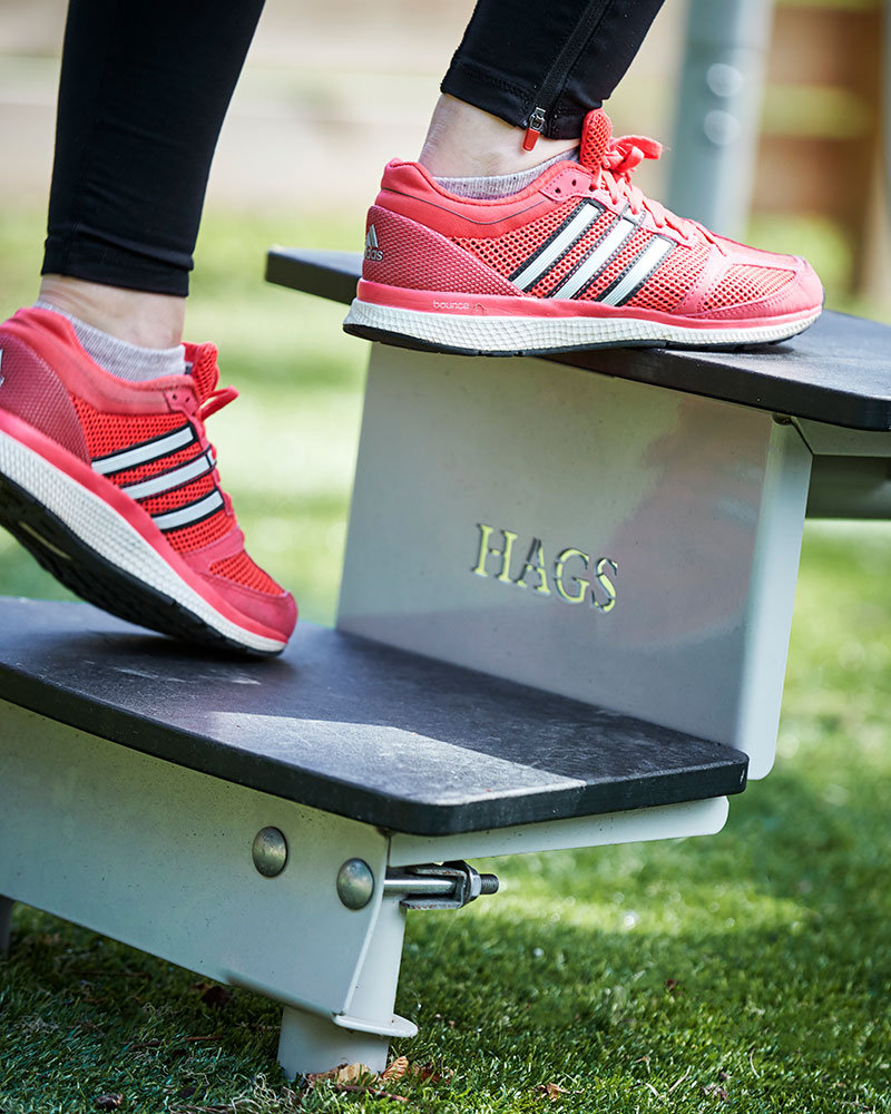 Close up of an outdoor exercise platform with stairs, it has a HAGS logo cut out on the steps, an person's feet is seen going up.